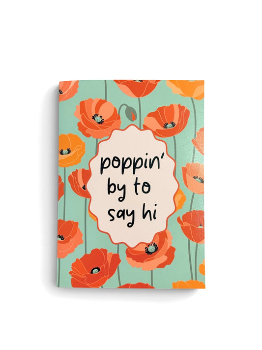 A greeting card with a floral poppy pattern in coral, orange, and peach on a light aqua background, featuring a central pink scalloped label with the handwritten text 'poppin' by to say hi'.