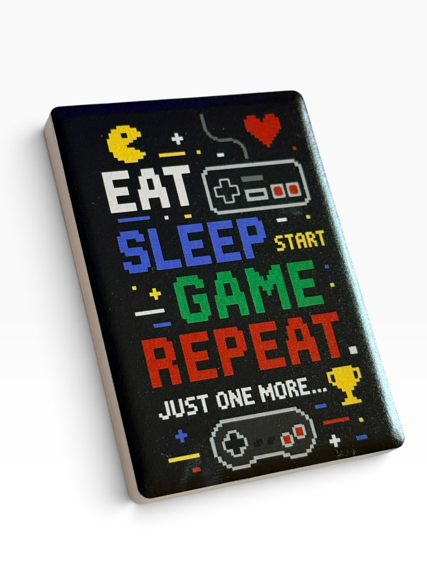 A rectangular ceramic magnet with colorful retro text reading 'EAT SLEEP START GAME REPEAT JUST ONE MORE.