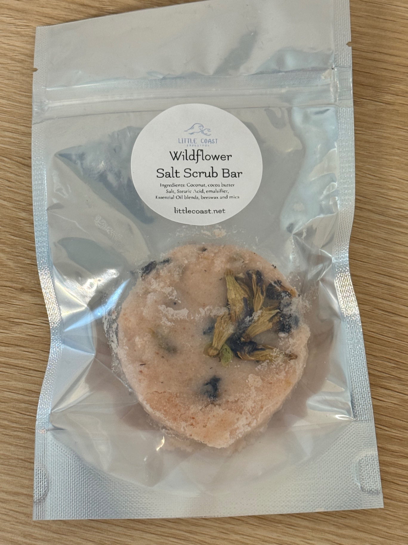 Wildflower salt scrub bar in a clear packaging on a wooden surface