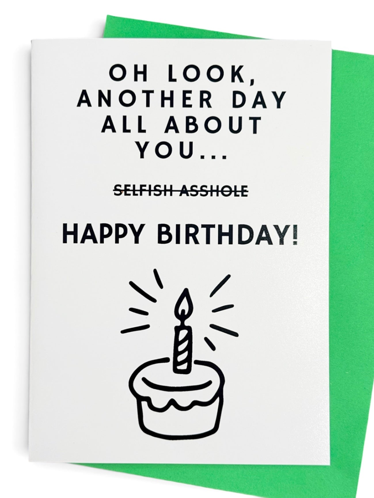 A white greeting card with black text that reads 'OH LOOK, ANOTHER DAY ALL ABOUT YOU with the words SELFISH ASSHOLE crossed out then a HAPPY BIRTHDAY greeting and an illustration of a cake with one candle burning. Shown with a green colored envelope behind it.