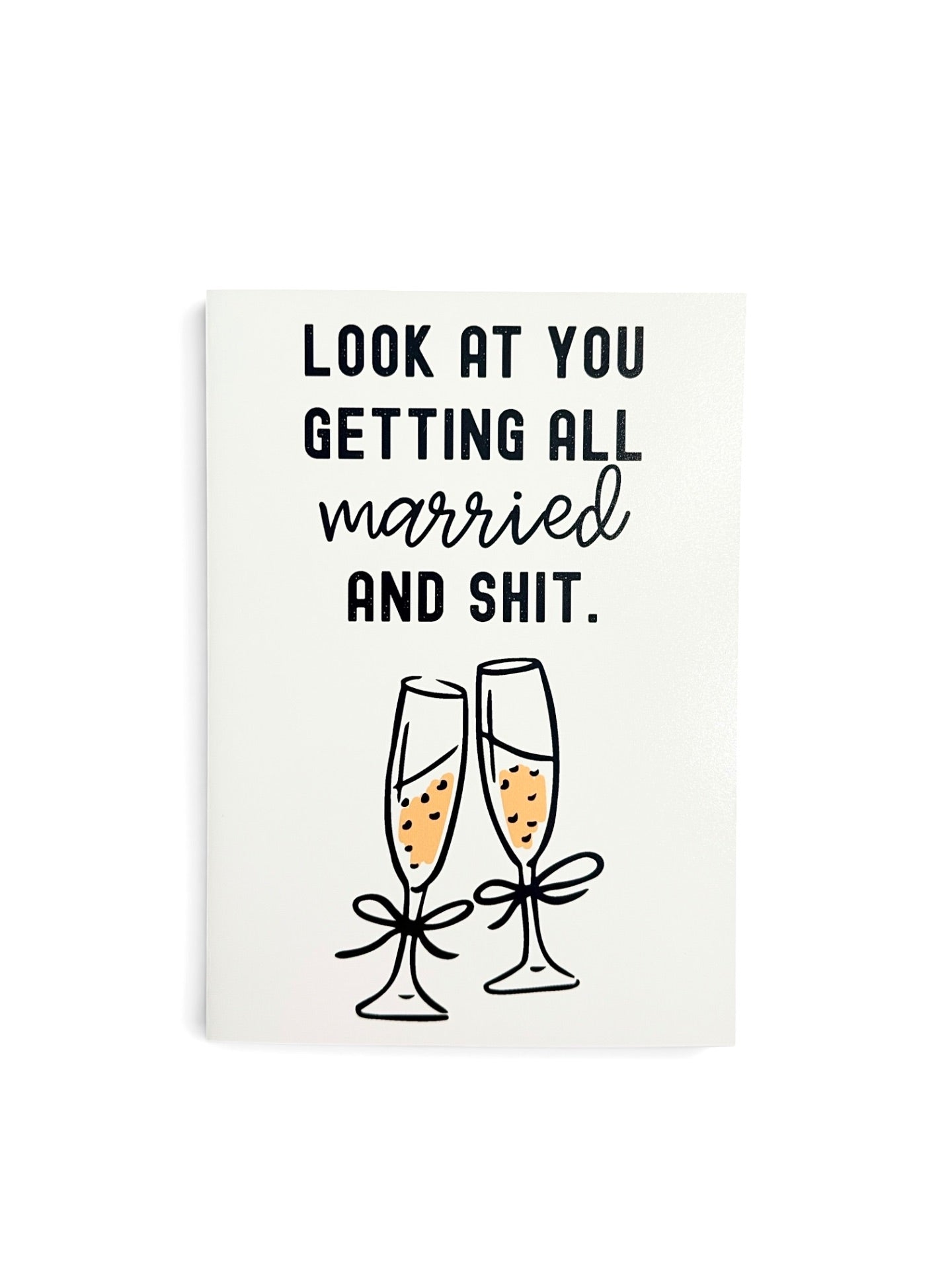 A white greeting card with black text reading 'LOOK AT YOU GETTING ALL married AND SHIT.' above an illustration of two champagne flutes with yellow champagne and black bows.