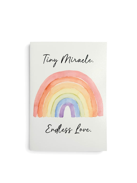 A white rectangular card featuring a watercolor rainbow in soft pastel shades with the words 'Tiny Miracle.' above and 'Endless Love' below.