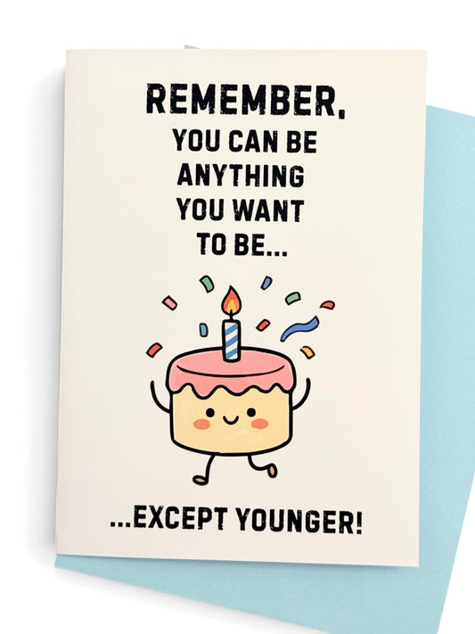 A white greeting card with a cute cartoon birthday cake character and the text 'REMEMBER, YOU CAN BE ANYTHING YOU WANT TO BE..' above the cake then text 'EXCEPT YOUNGER' below the cake. Shown with a light blue colored envelope behind the card.