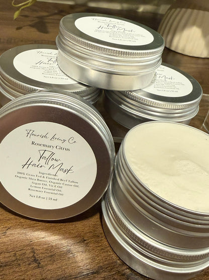 Several round silver metal tins of hair masks are arranged on a wooden surface. One tin is open, showing a white cream product, while others are closed with white labels.