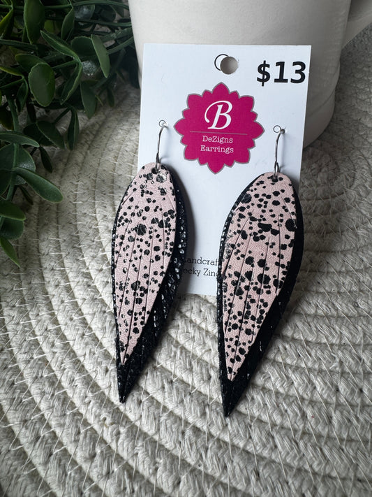 A pair of long teardrop-shaped dangle earrings with a light pink background and black speckled pattern, hanging from silver hooks on a white display card. The card shows the brand 'B Designs Earringz' and a price of '$13'.