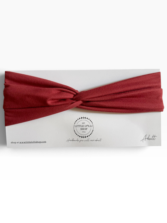 A knotted headband in a brick red color, presented on a white backing card with the brand name 'Little Lolli Shop' visible in the center.