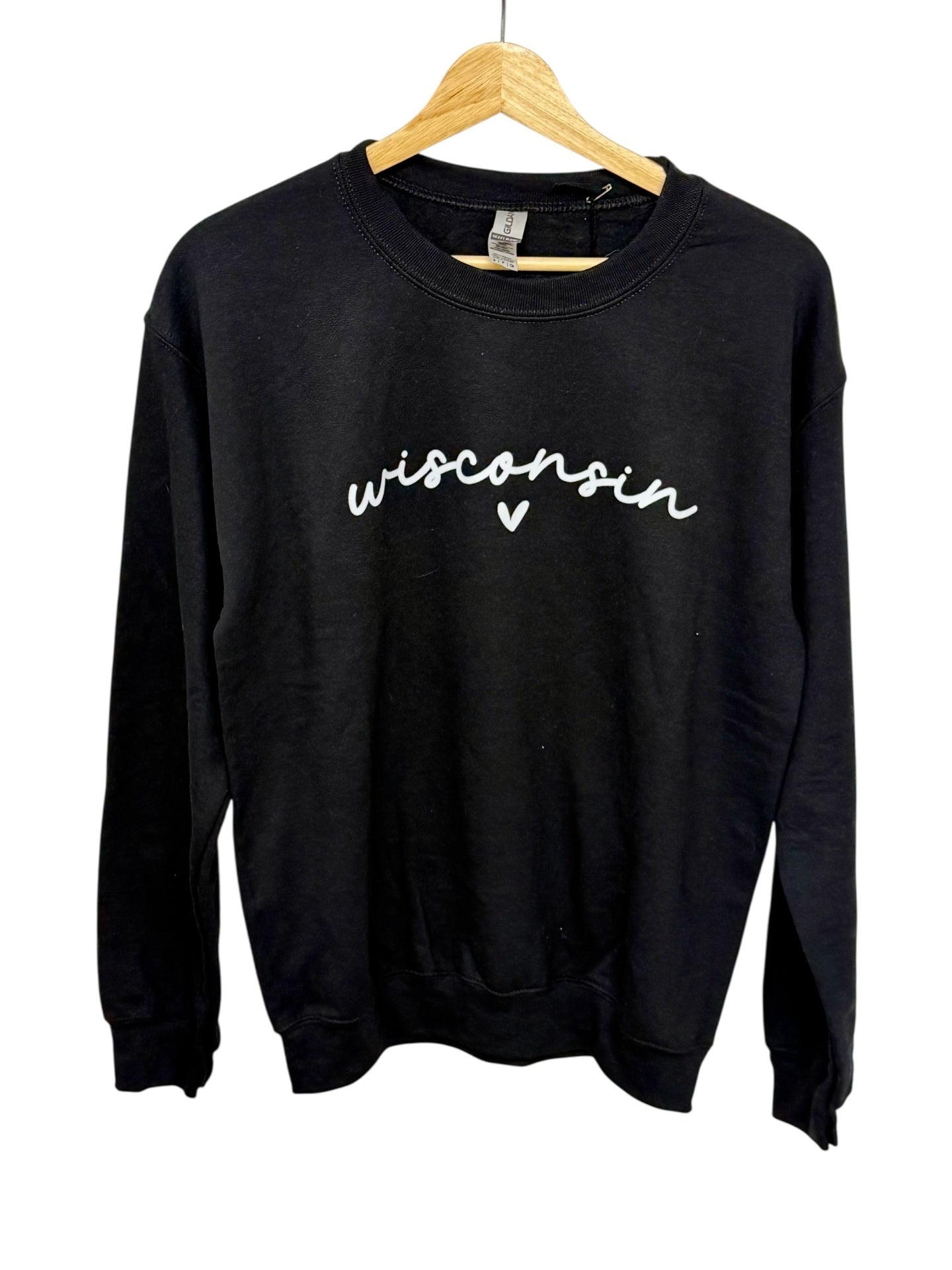 A black crewneck sweatshirt with 'wisconsin' written in white cursive script and a small heart below it, hanging on a wooden hanger against a white background.