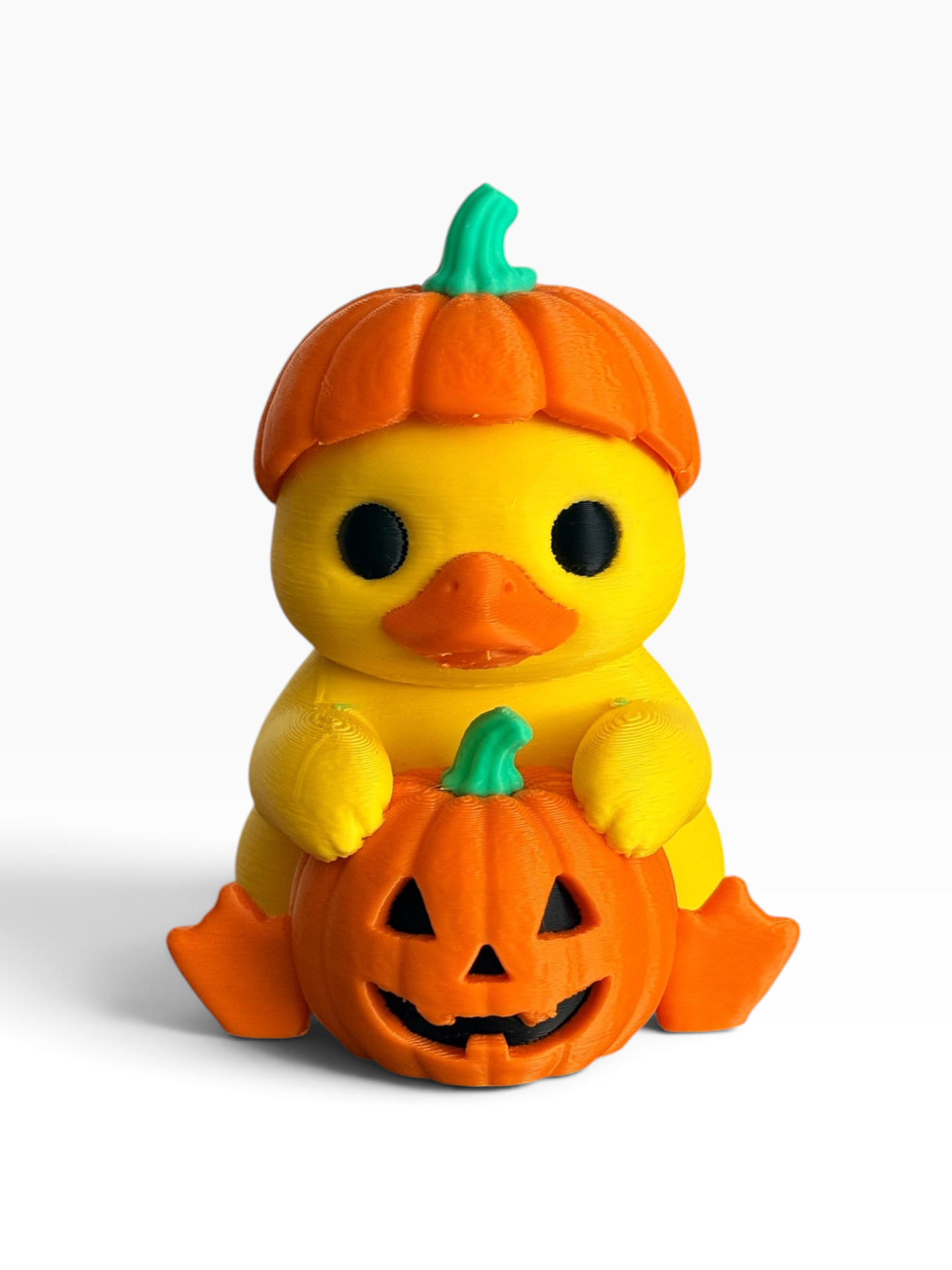 A 3d printed yellow duck toy styled as a baby duck wearing an orange pumpkin hat and holding a carved orange jack-o'-lantern pumpkin, set against a plain white background.
