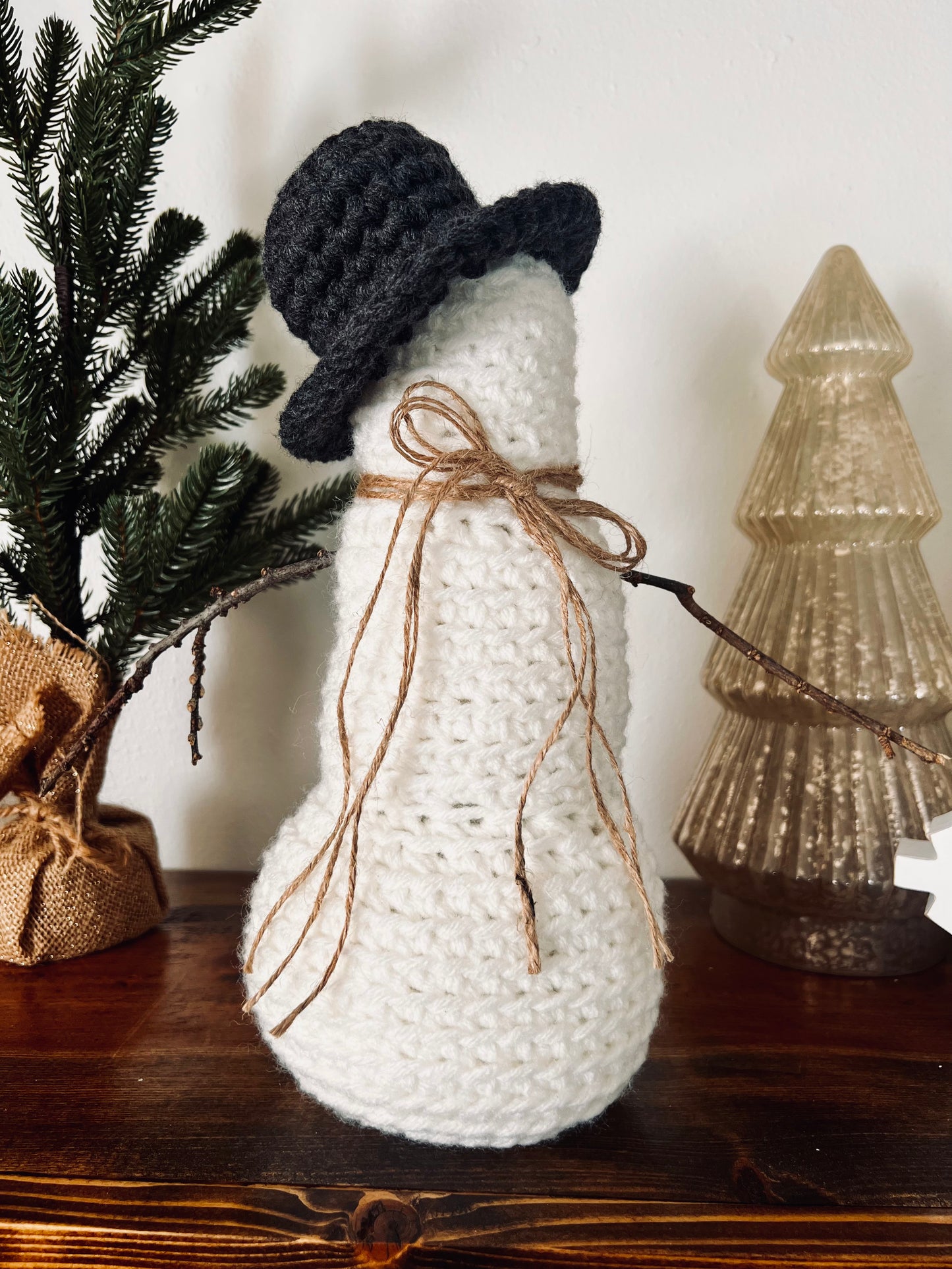 crocheted snowman on shelf with christmas decor behind it