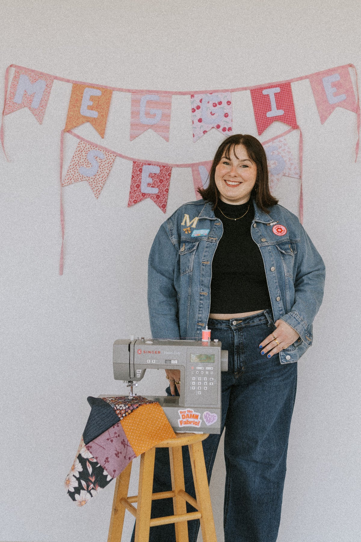 Woman standing next to a sewing machine with a 'Maggie is Sewing' banner in the background