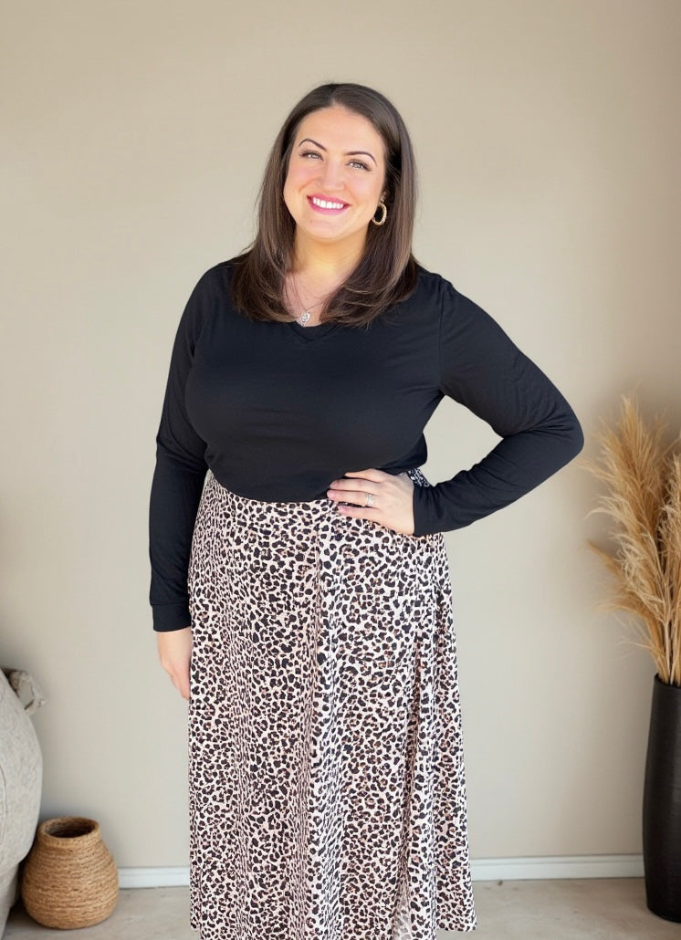 Woman wearing a black long-sleeve top and leopard print skirt indoors.