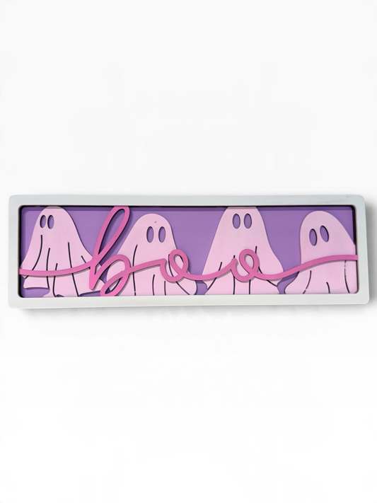 A rectangular Halloween wall sign with a white frame, featuring four light pink ghosts on a lavender-purple background with a pink cursive 'boo' script across the front.