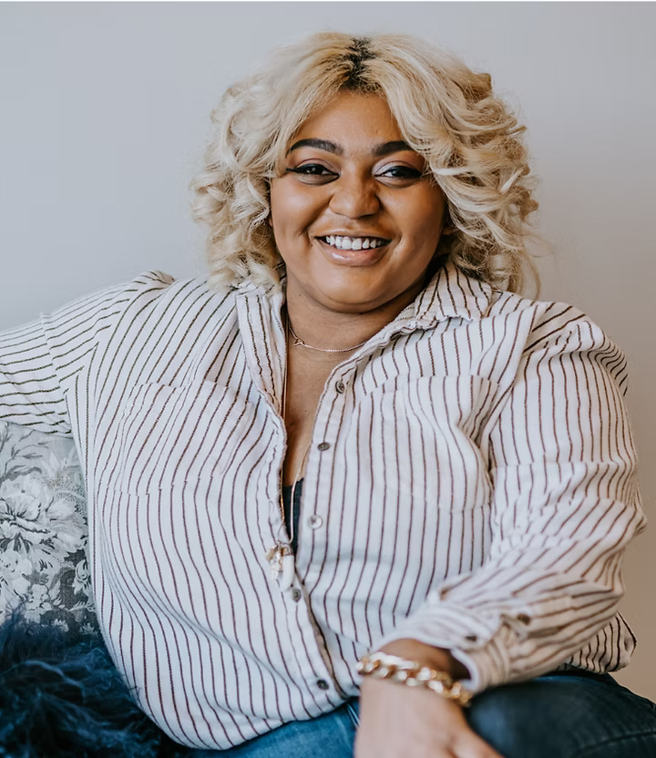 Woman with blonde hair wearing a striped shirt sitting on a couch.