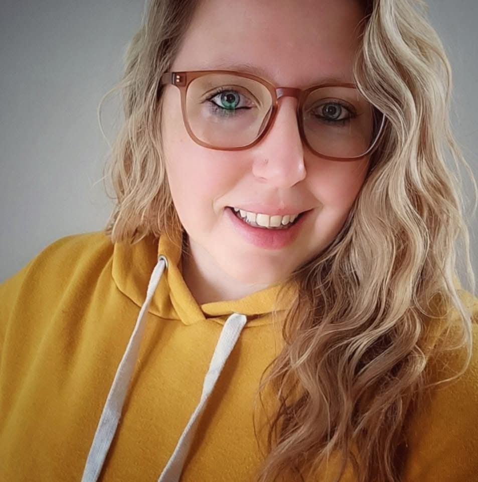 Person wearing glasses and a mustard yellow hoodie against a neutral background