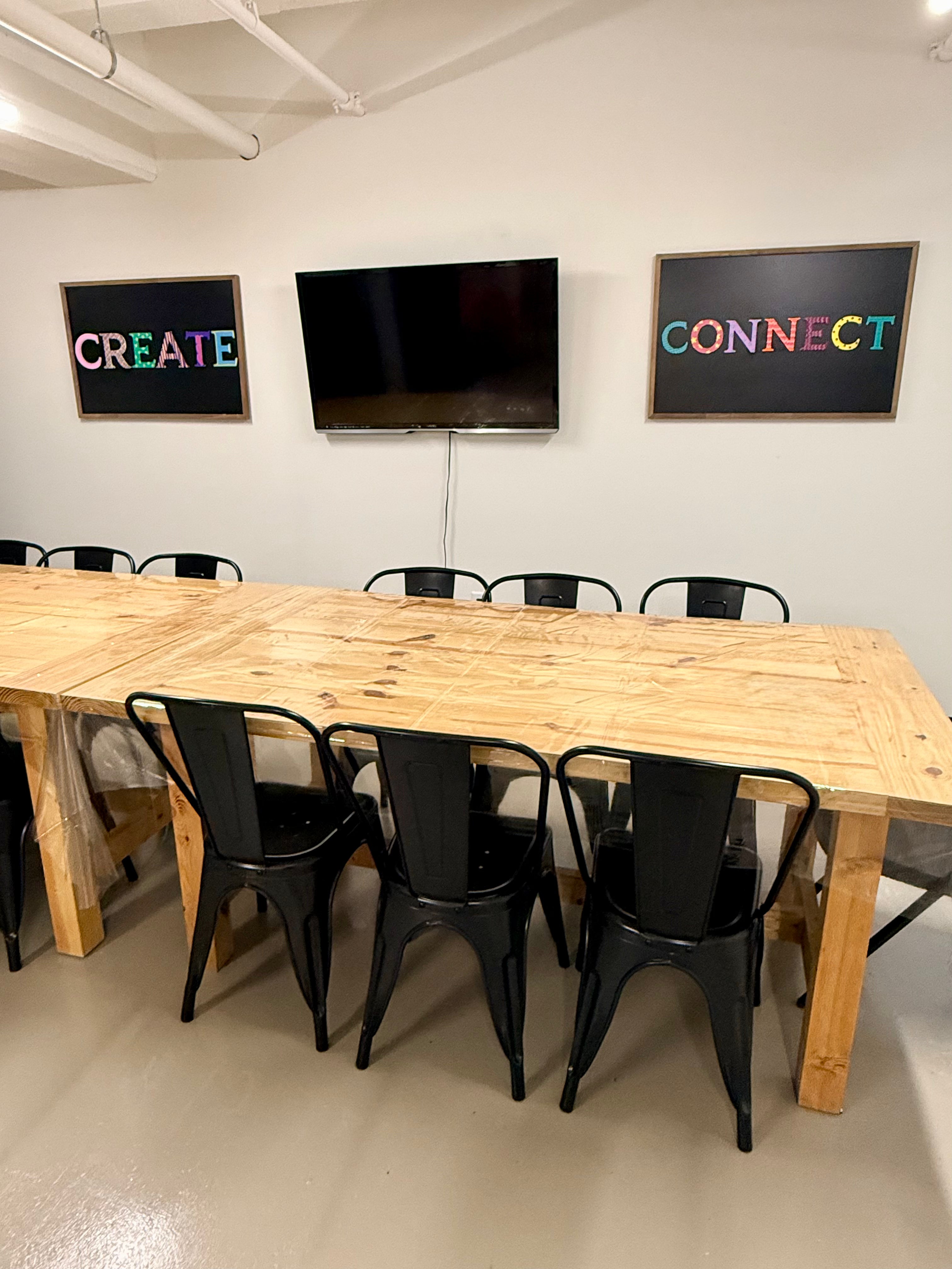 Wooden table and black chairs, featuring motivational words on chalk boards 'create' on one and 'connect' on the other with a tv in the middle.