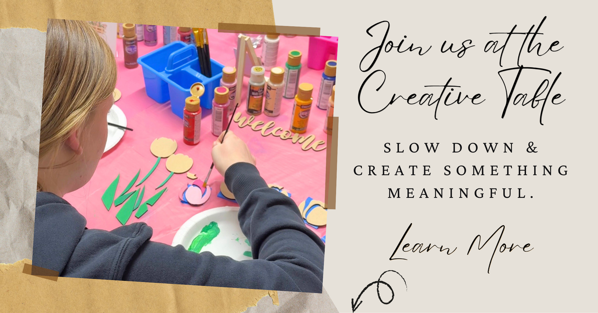 Promotional graphic with a photo of a woman painting at a pink table surrounded by craft supplies, next to text that reads 'Join us at the Creative Table' and 'Slow down & create something meaningful. Learn More'.