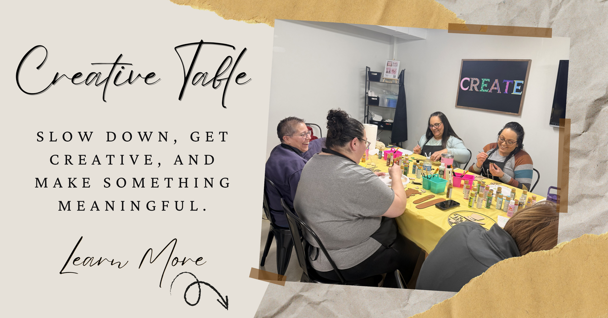 Group of people engaged in a creative activity at a table with text 'Creative Table' and motivational quote reading 'slow down, get creative and make something meaningful. learn more' with arrow pointing to the next section.