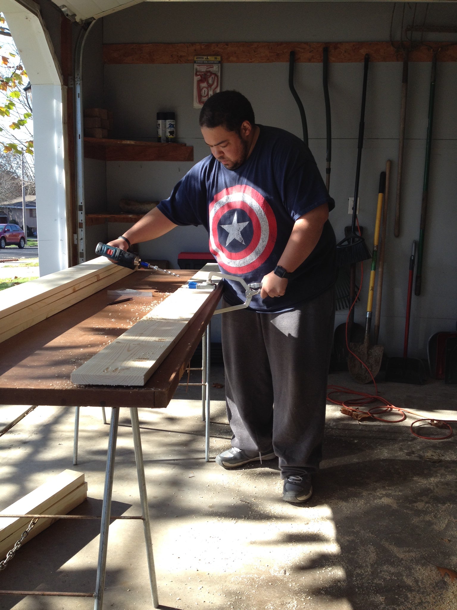 A photo of a man standing next to a table working on a wood project holding tools. 