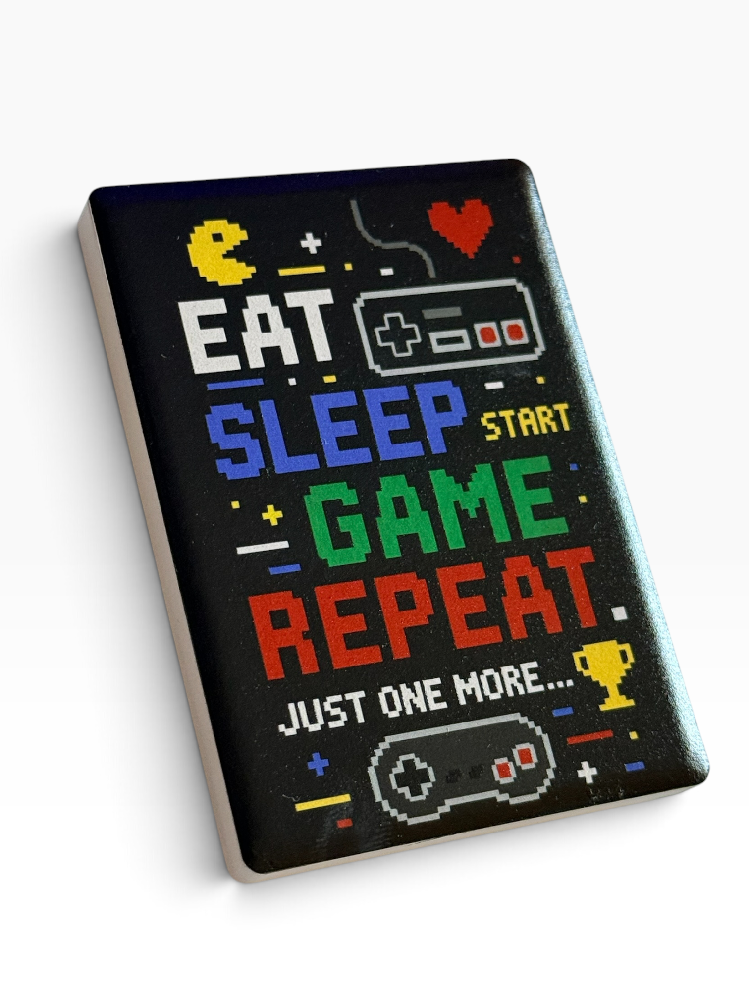 A rectangular ceramic magnet with colorful retro text reading 'EAT SLEEP START GAME REPEAT JUST ONE MORE.