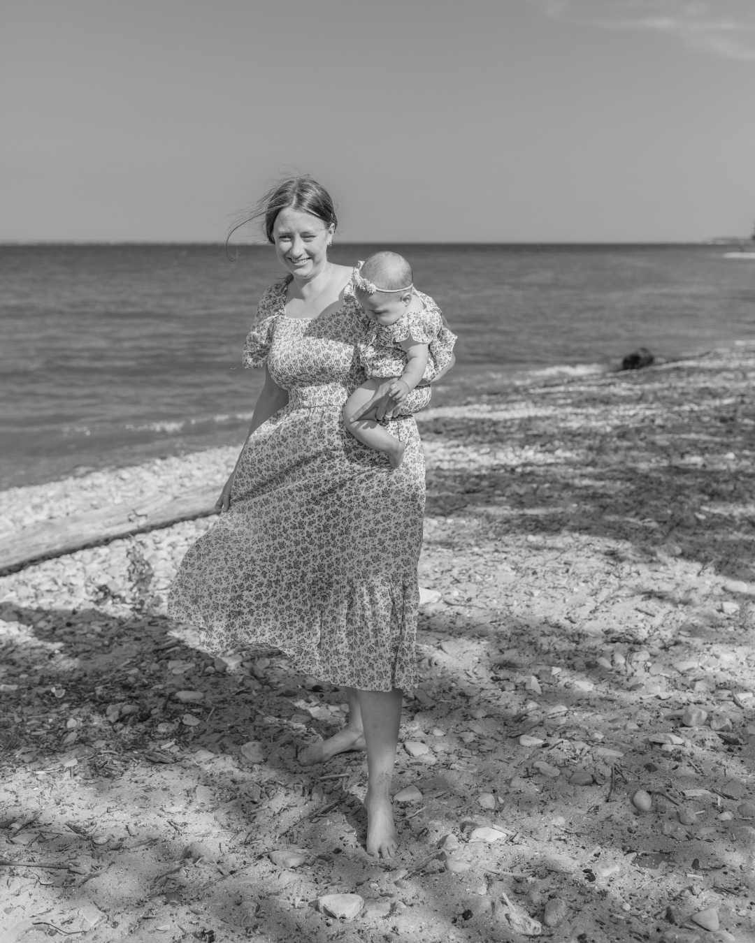 Woman in a floral dress holding a baby on a beach