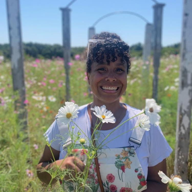 Woman holding flowers in a field with a wooden fence and blue sky in the background