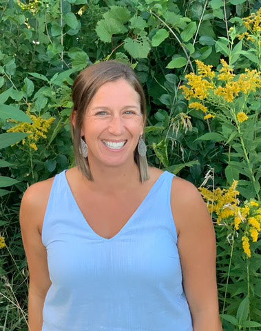 Woman in a light blue dress standing in front of green foliage and yellow flowers