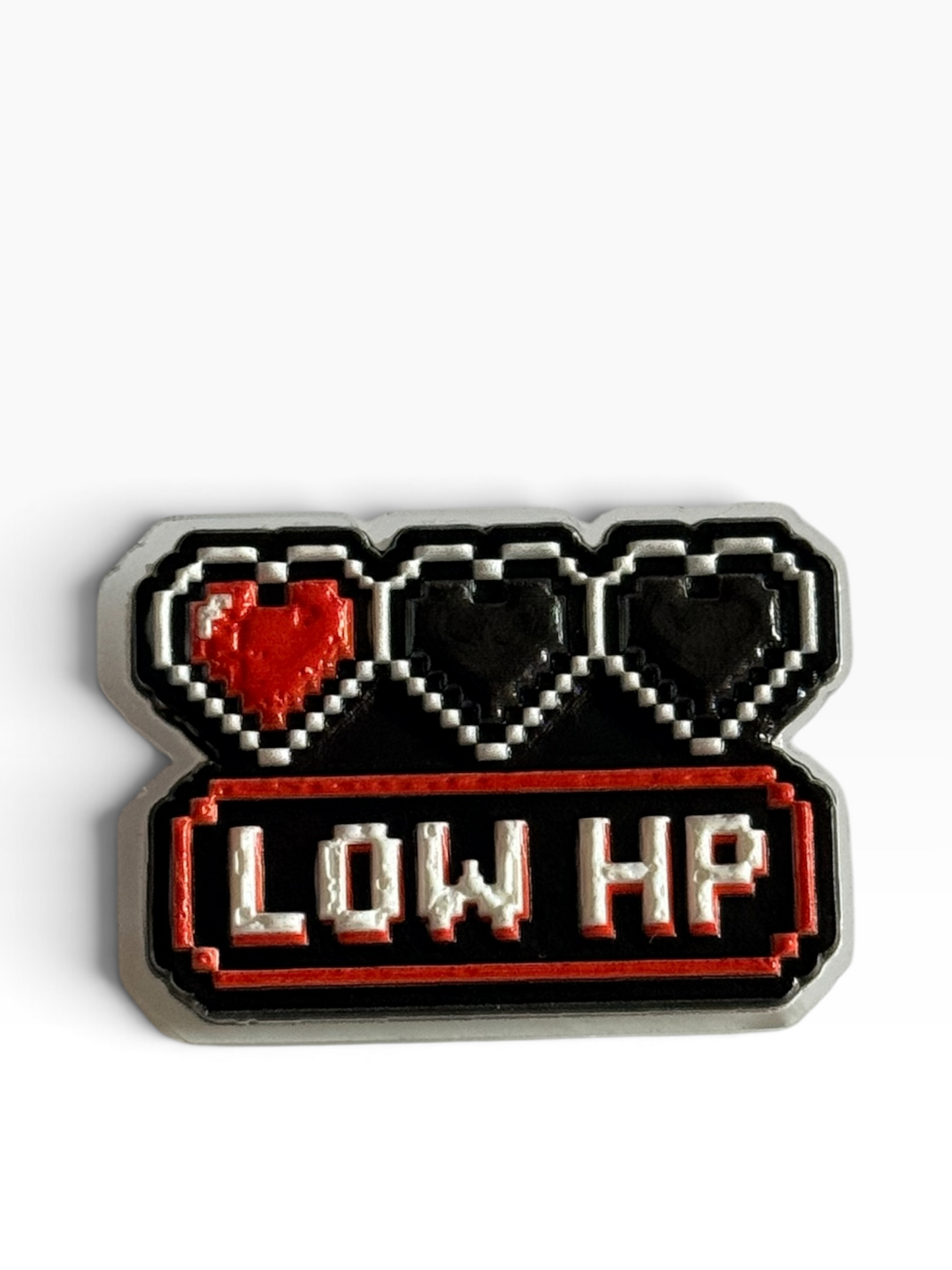 A pixel art acrylic uv printed pin featuring three hearts with one red heart and two black hearts, above a red bar with the text 'LOW HP' in white, on a white background.