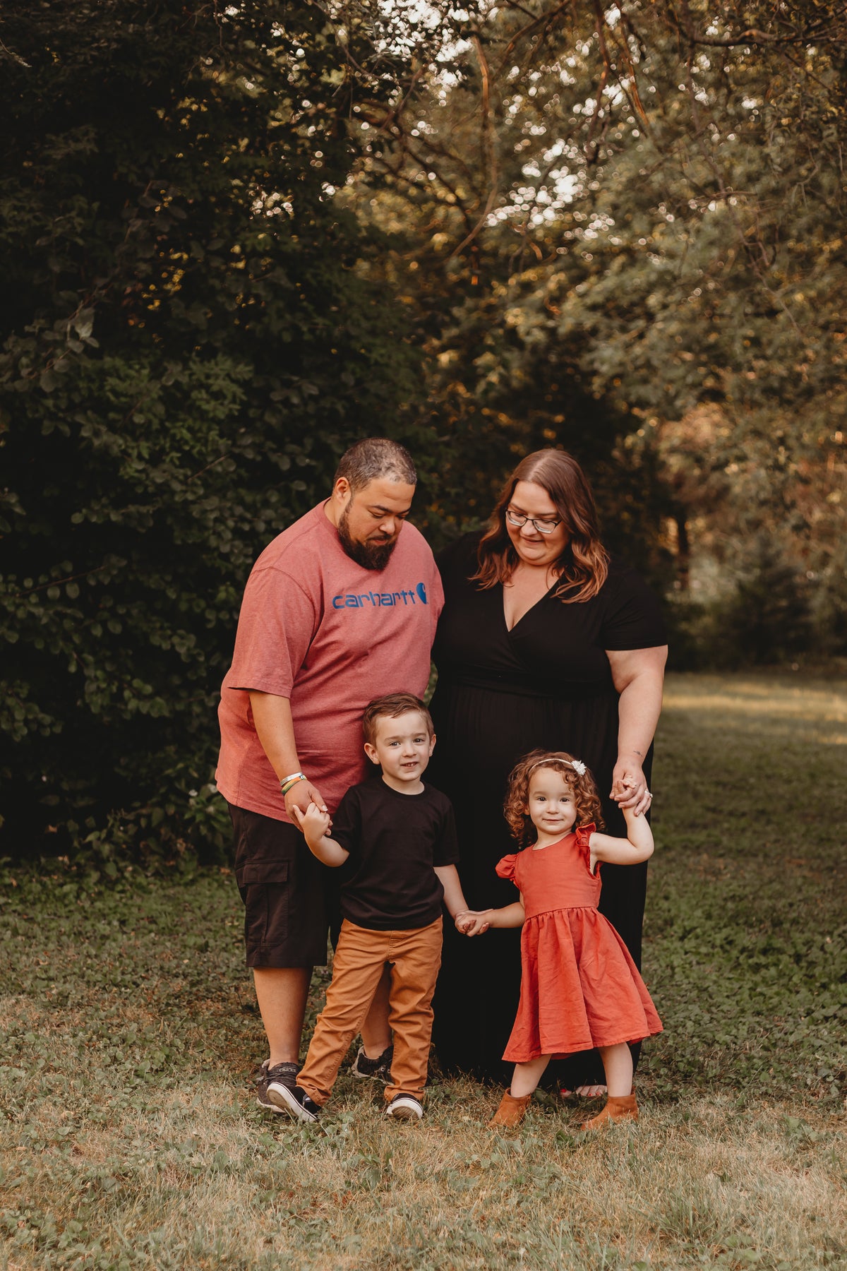 Family of four standing together for a picture. Two adults and two children all holding hands. 