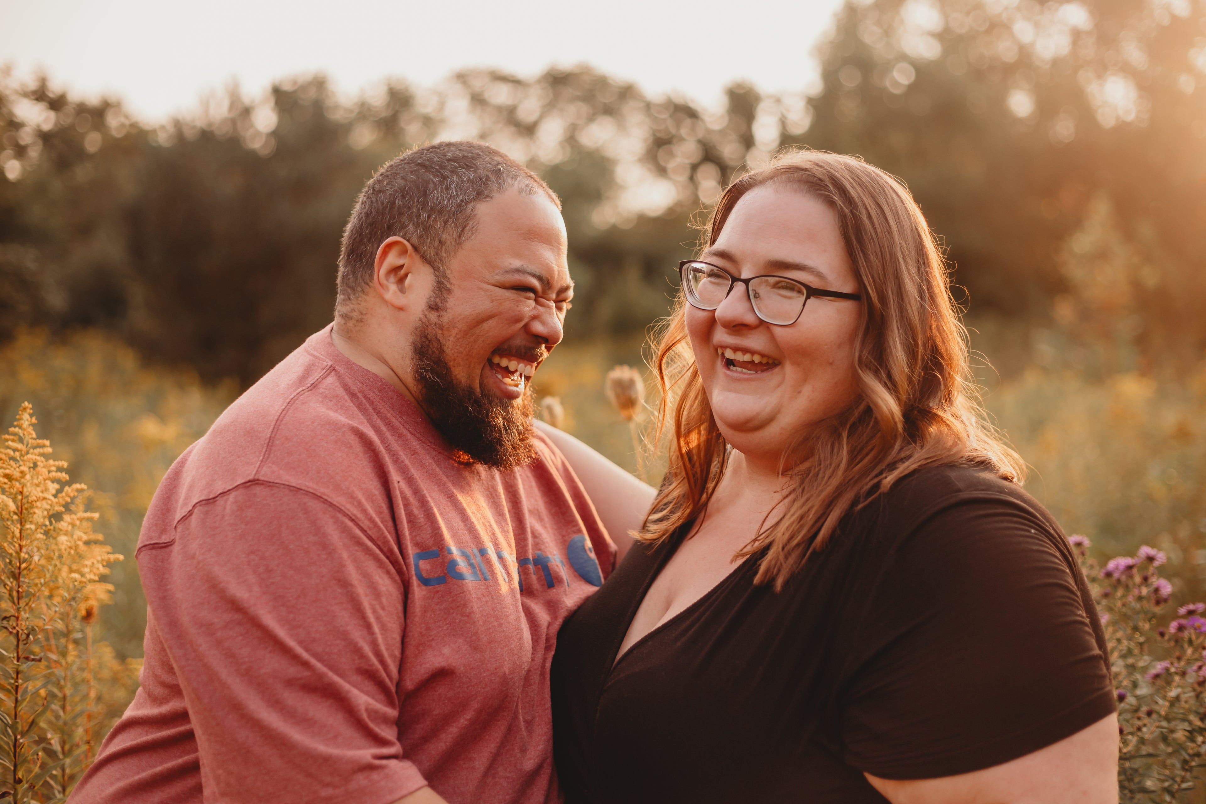 A photo of a man and woman holding onto each other, both are laughing and smiling.