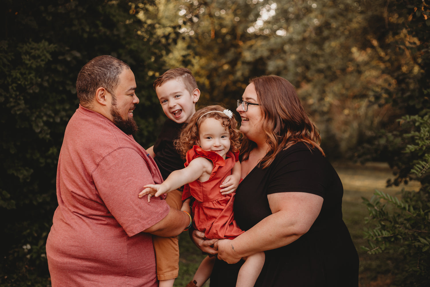 Photo of a family of four, two adults two children laughing and smiling. The parents are on the outer sides holding the children in the middle.