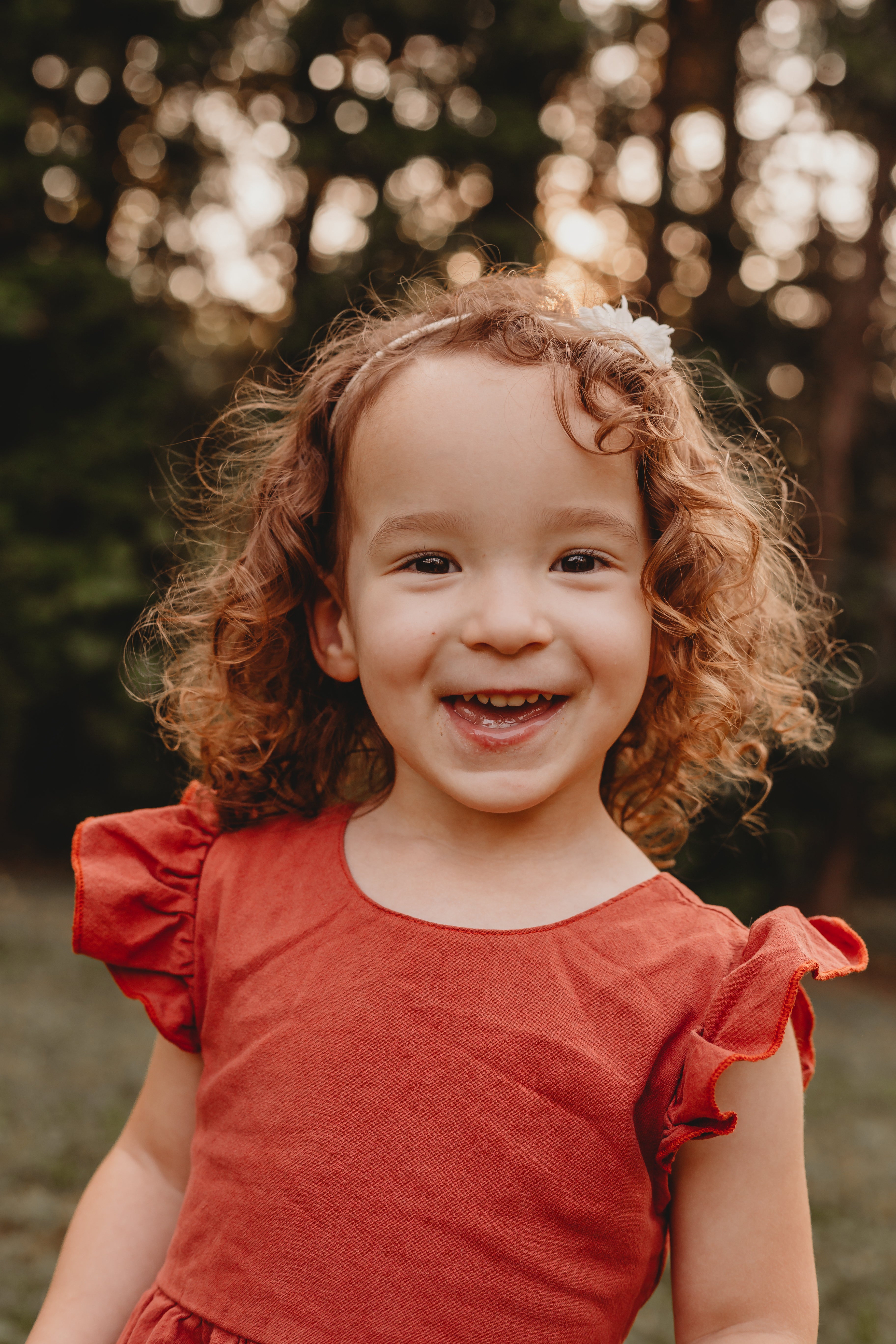Photo of a young girl with curly hair wearing a orange colored dress smiling at the camera.