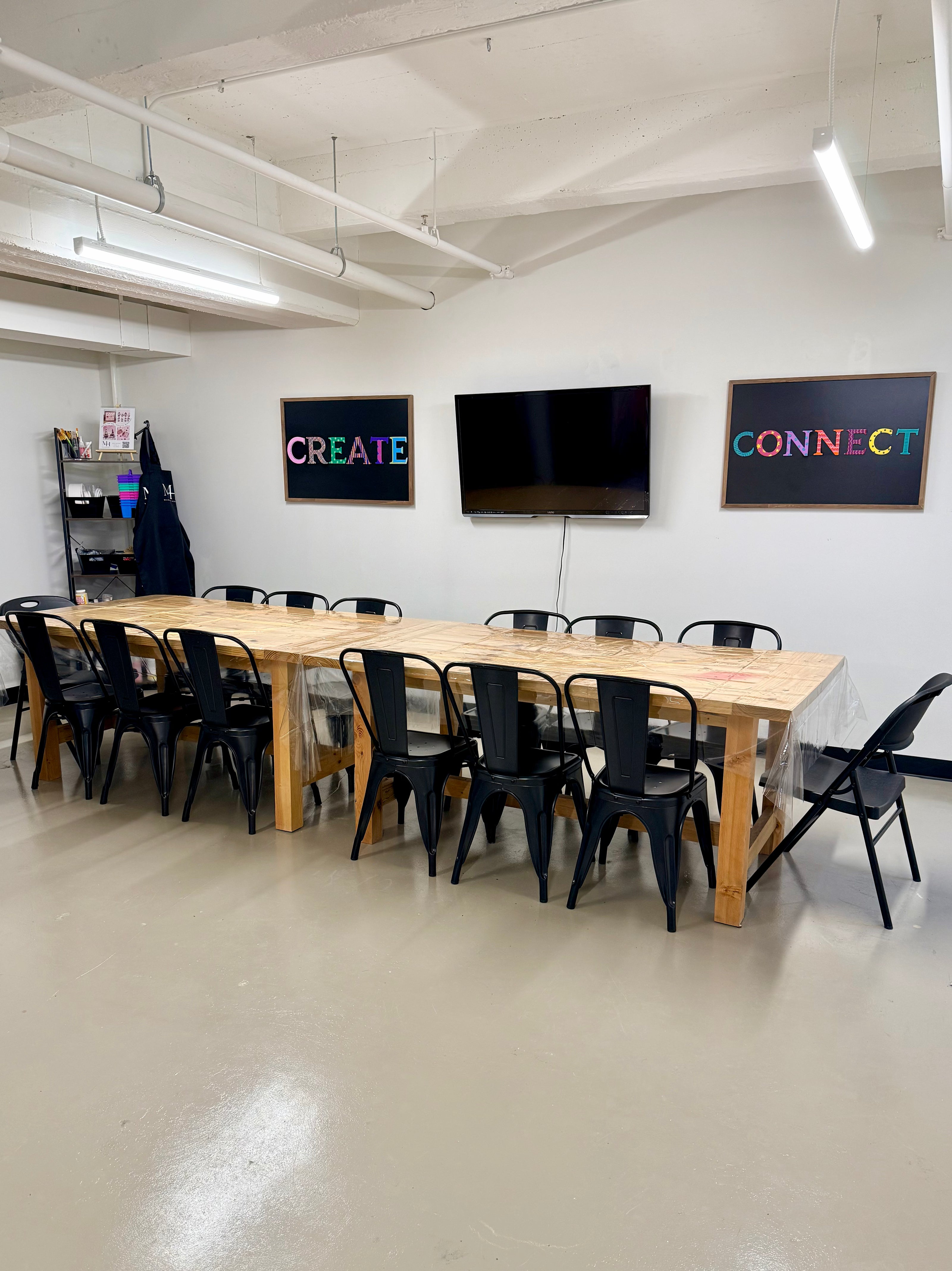 Workshop classroom space with long wooden table and black chairs, featuring motivational wall art with text 'create' and 'connect'