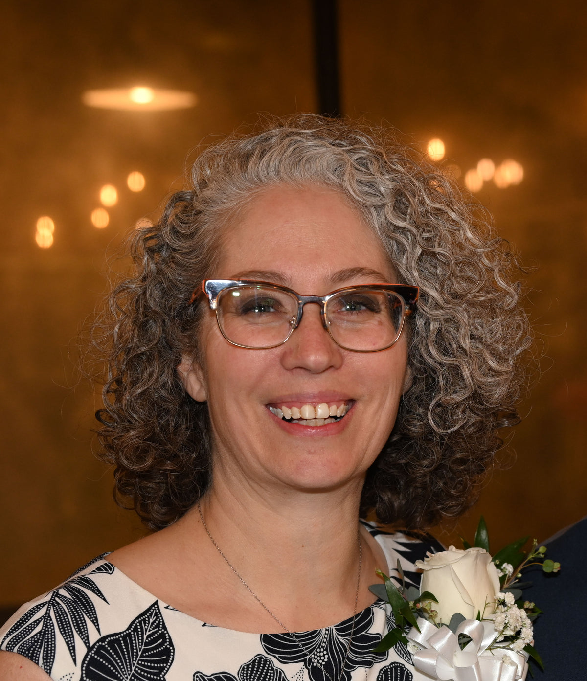 Woman with gray hair and glasses smiling in front of a warm-toned background