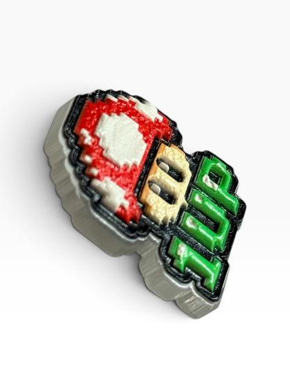 A side view of an acrylic uv printed pin featuring the text '1UP' in green and beige, with a red and white pixelated mushroom cap design, shown on a white background.