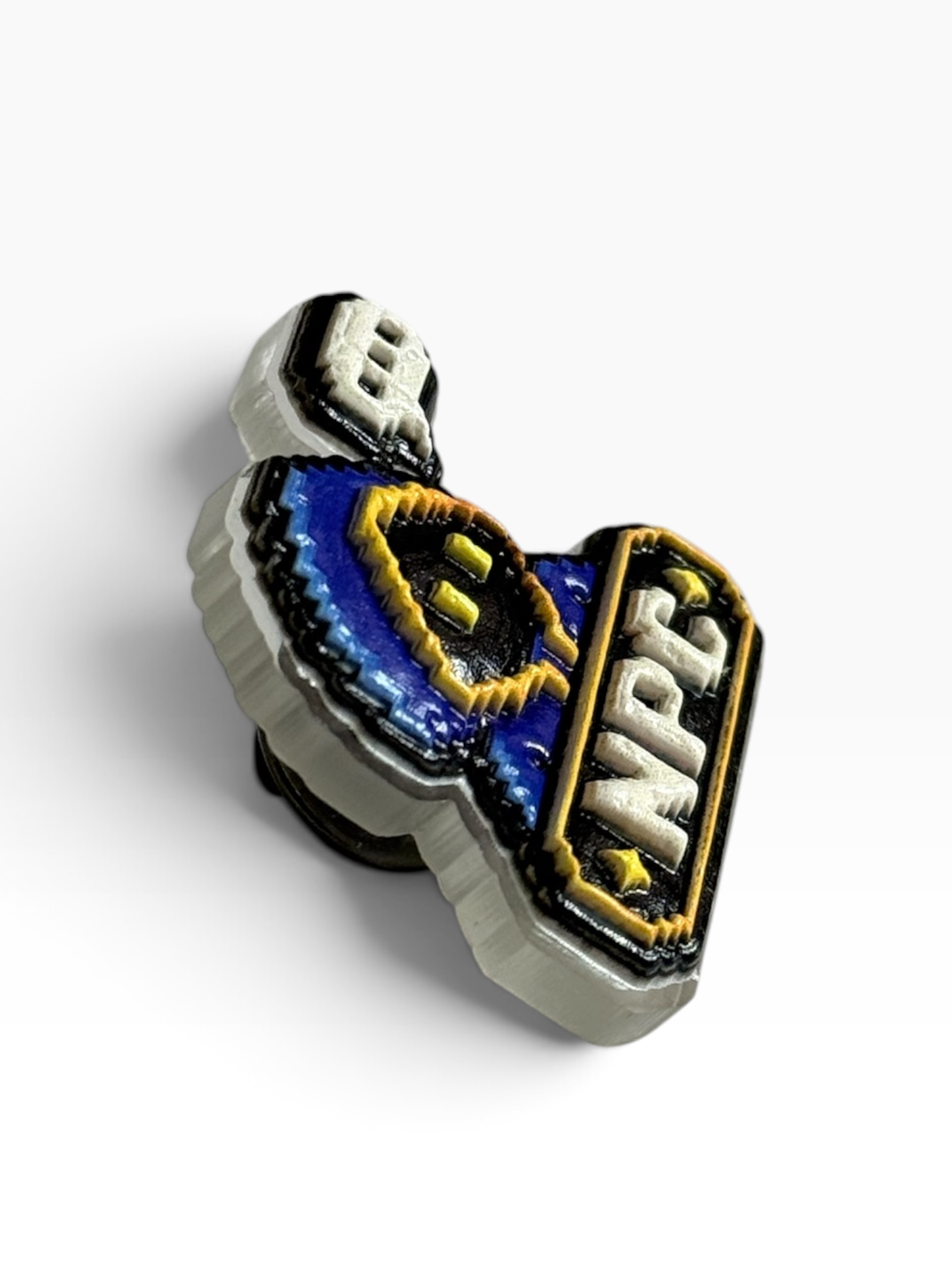 A close-up of a small acrylic uv printed pin with a clear outer border, blue and yellow central design, and white lettering reading 'NPC' on a white background.