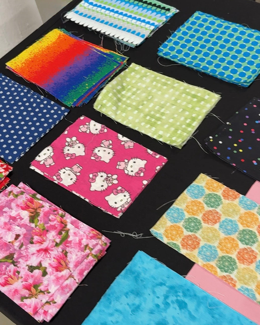 A collection of colorful fabric swatches with various patterns including polka dots, florals, stripes, and cartoon prints, arranged on a black surface.