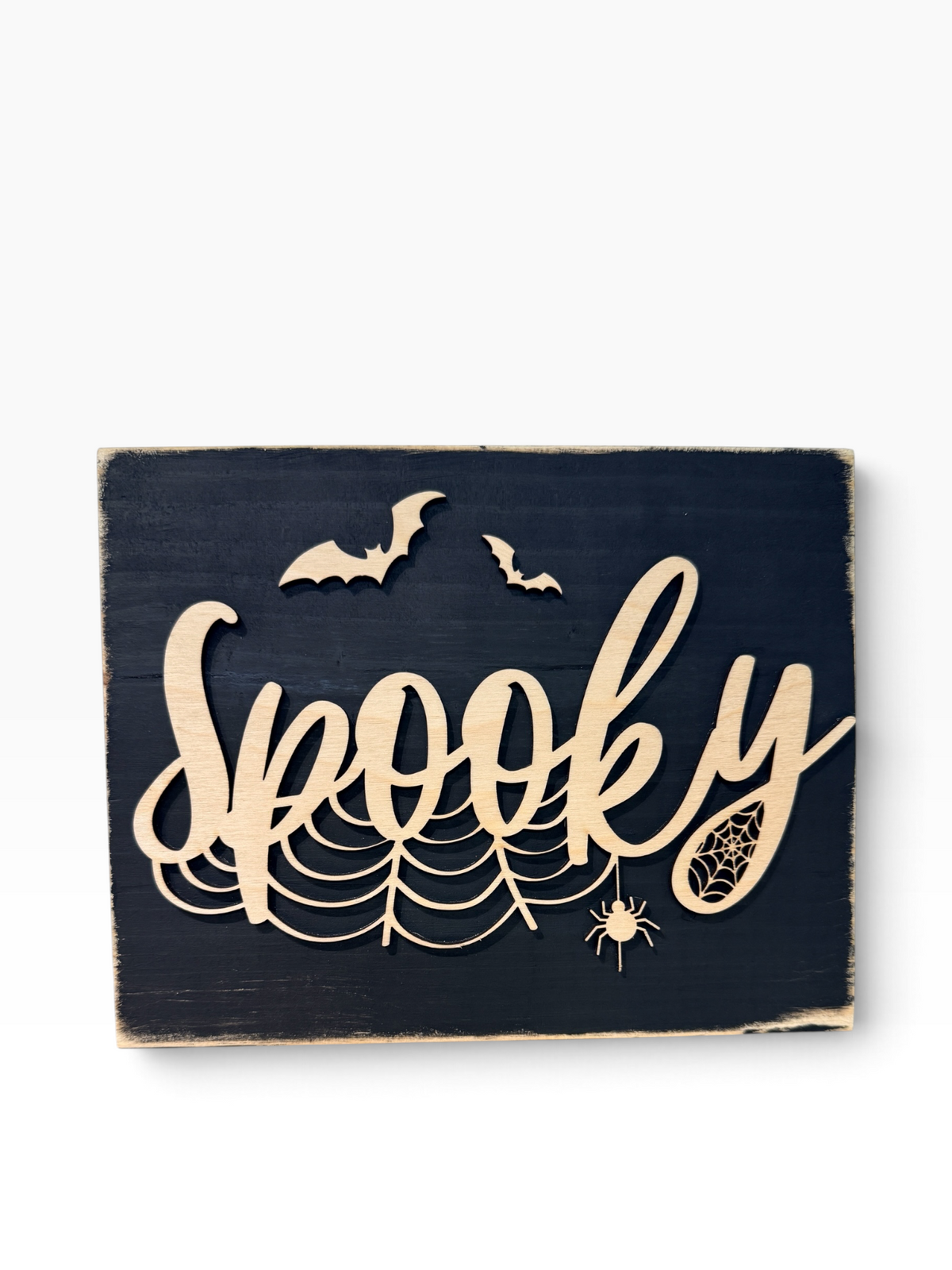 Laser cut bat motifs and the word "Spooky" in a light wood on a black sign with distressed edges. Displayed on a white background. 