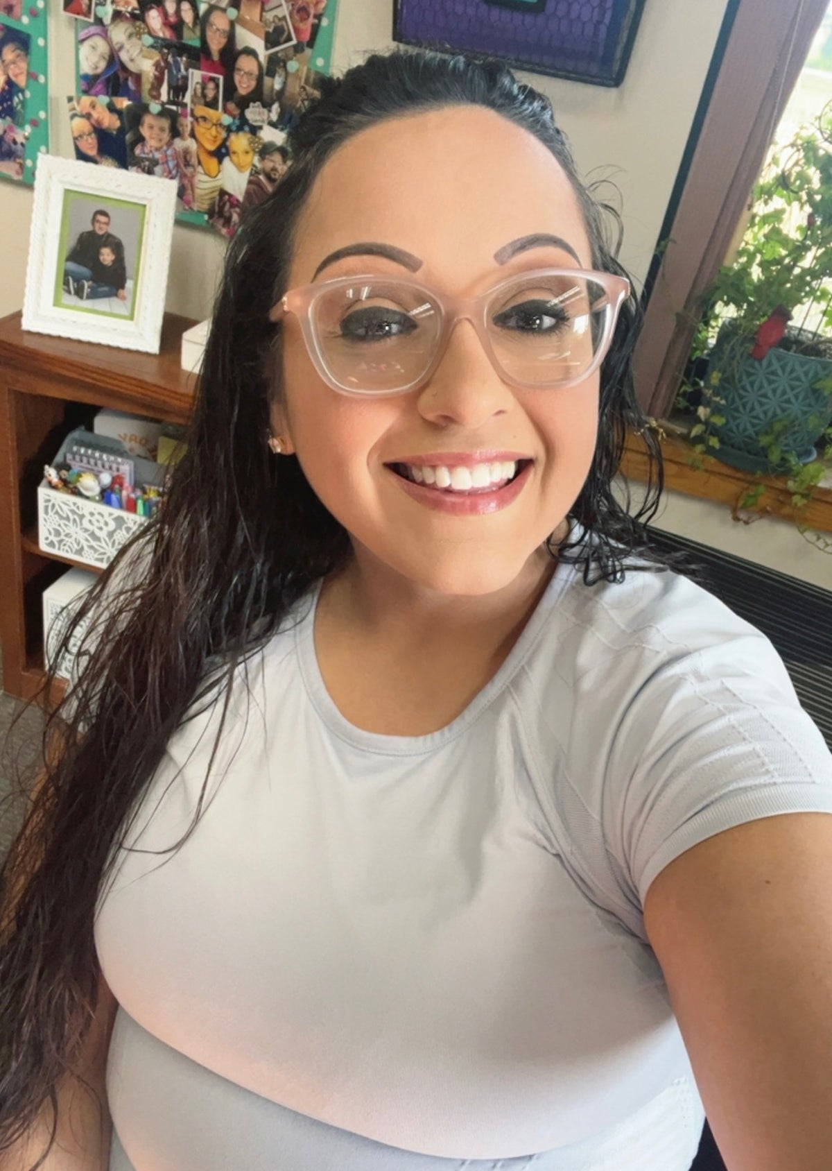 Woman wearing glasses and a white shirt in an indoor setting with a bookshelf and window in the background.