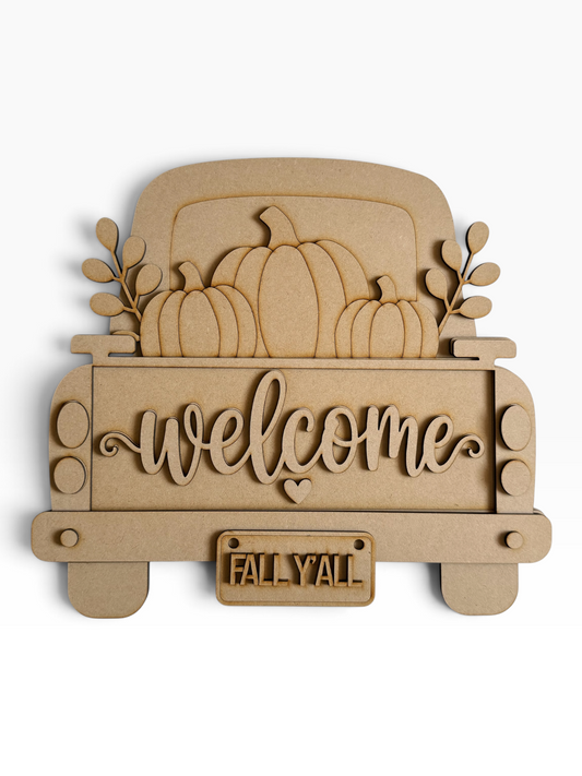 A laser-cut mdf decorative sign shaped like the back of a pickup truck carrying pumpkins, with the word "welcome" in script across the bed and a small license plate reading "FALL Y'all" on a white background.