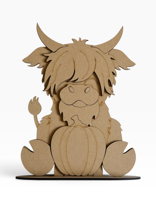 A laser-cut mdf Highland cow shelf sitter and pumpkin decoration on a white background.