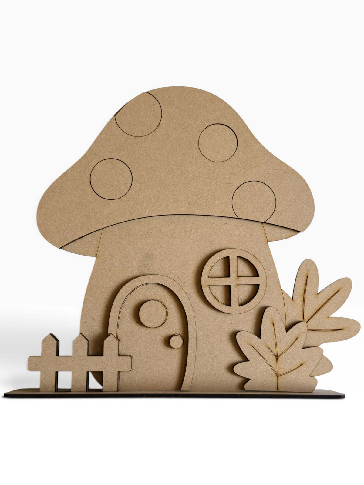 A fall themed unfinished MDF decorative cutout of a mushroom house with a small fence and leafy plants, shown on a clean white background.