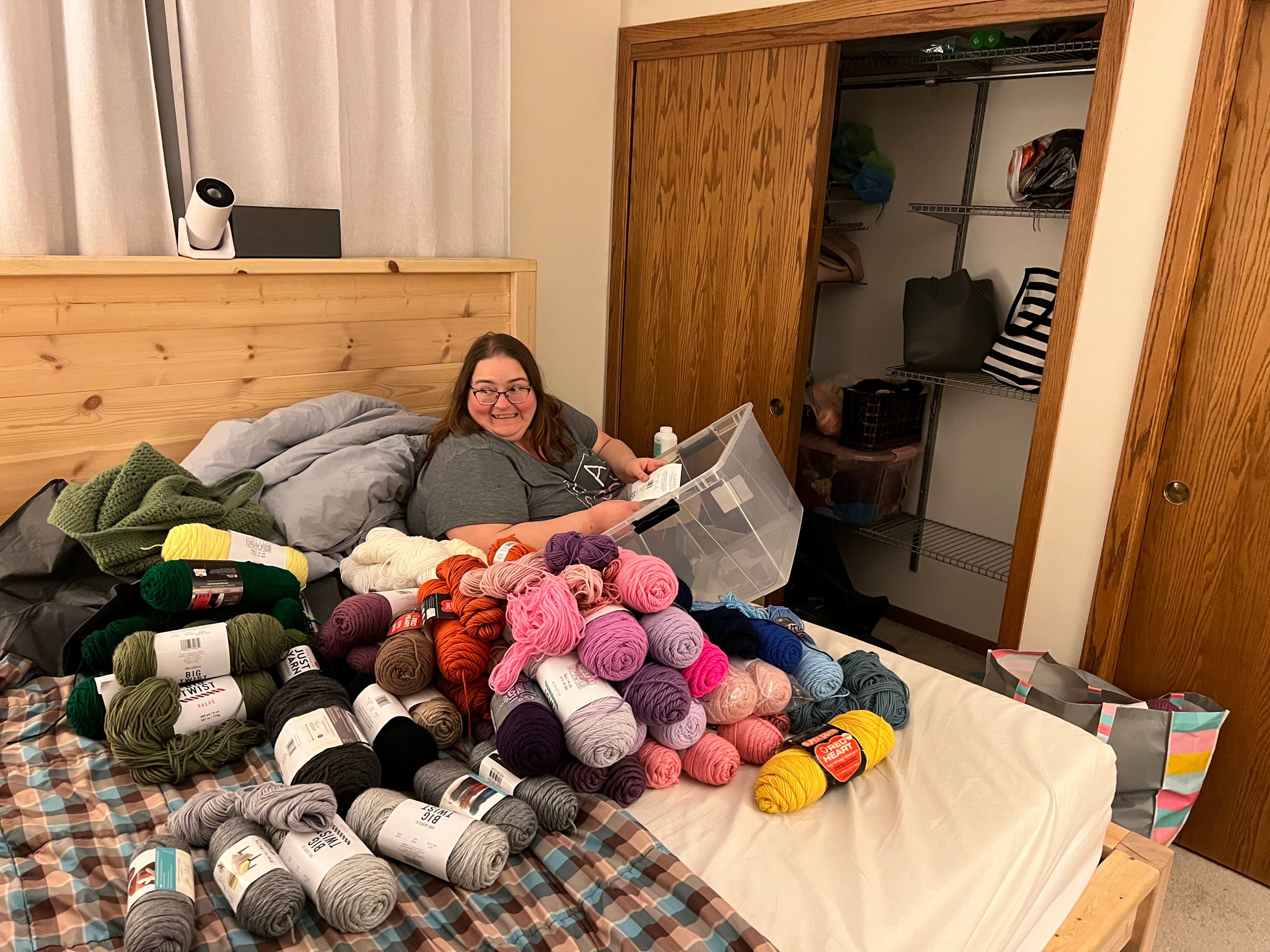 A photo of a woman sitting on a bed with a collection of yarn strewn over the bed space. 